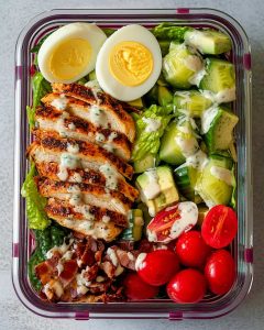 Cobb salad meal prep box filled with grilled chicken, avocado, tomatoes, cucumber, bacon, and a hard-boiled egg.