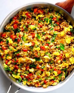 Fried rice meal prep featuring scrambled eggs, red peppers, green onions, peas, and brown rice.
