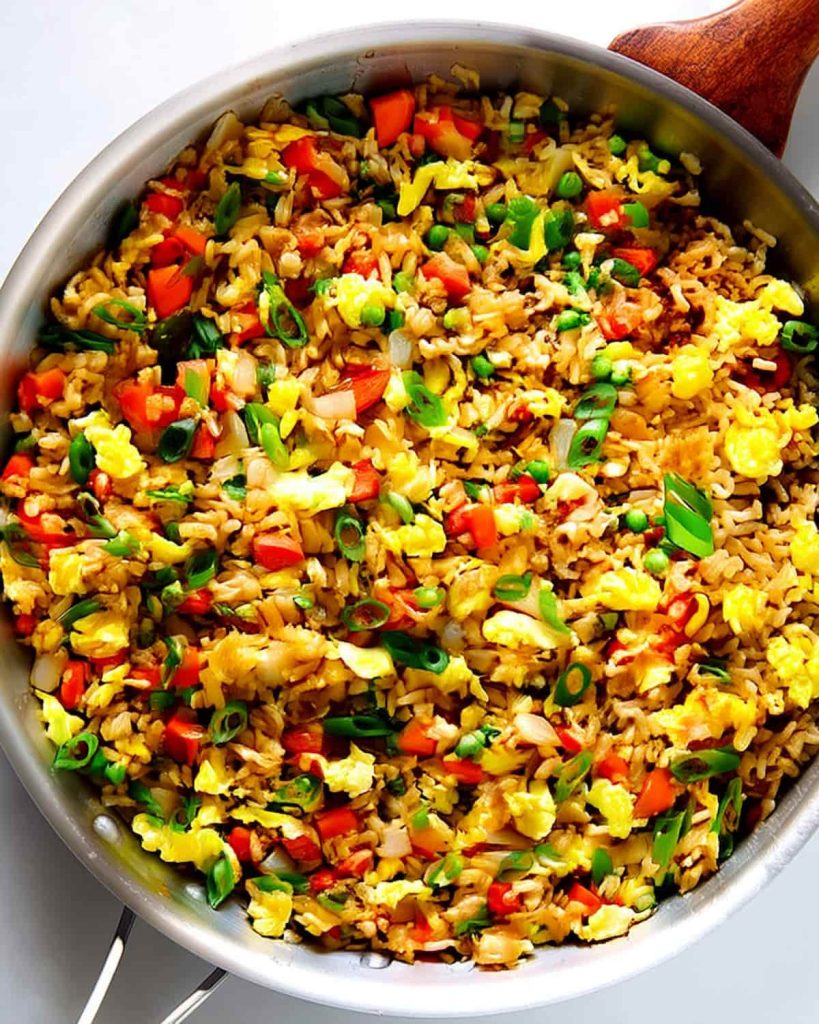 Fried rice meal prep featuring scrambled eggs, red peppers, green onions, peas, and brown rice.