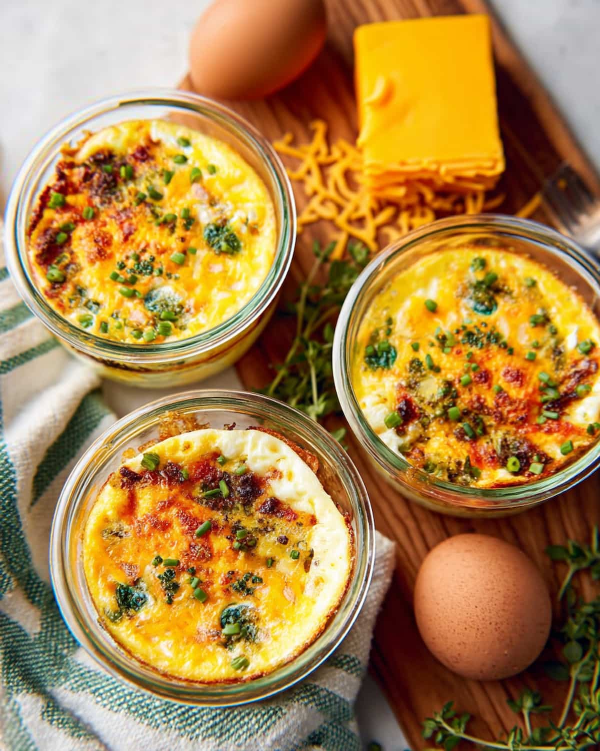 Meal prep egg bake with melted cheese, fresh herbs, and crispy edges, displayed with eggs.