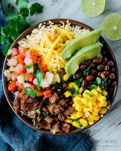 Taco bowls meal prep with seasoned beef, rice, black beans, corn, cheese, pico de gallo, avocado.