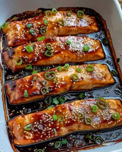 Plate of teriyaki salmon meal prep with glazed salmon fillets topped with sesame seeds and green onions in a rich.