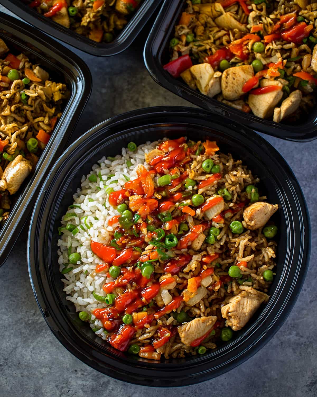 Chicken fried rice meal prep bowls with white rice, diced chicken, peas, carrots, and red sauce.