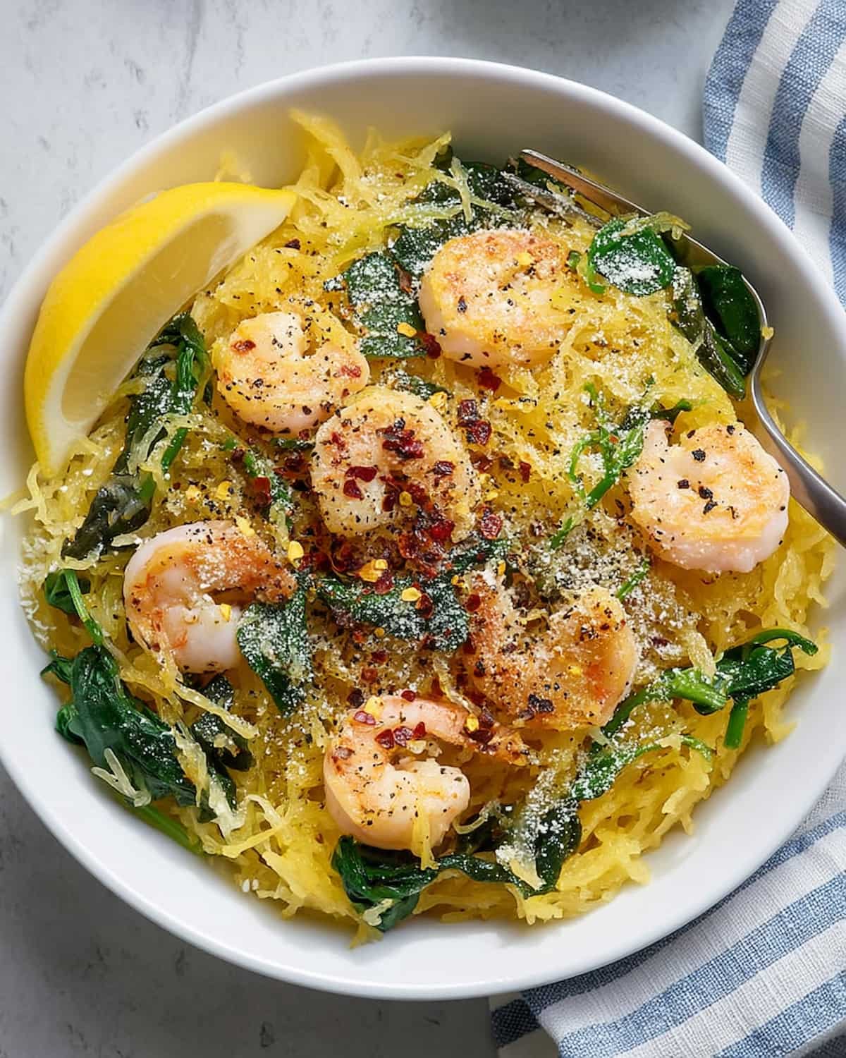 Shrimp scampi spaghetti squash meal prep with juicy shrimp, tender squash strands, garlic, spinach, lemon, and a sprinkle of parmesan cheese.