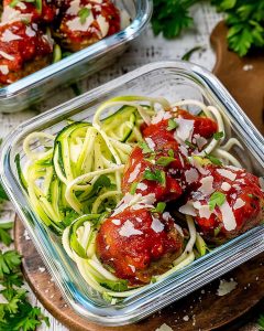 Glass meal prep container with turkey meatballs zoodles bowls, topped with marinara sauce, Parmesan shavings, and fresh parsley.