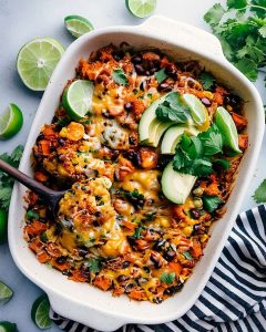 Enchilada Quinoa Bake with black beans, melted cheese, sweet potatoes, and quinoa, topped with avocado, cilantro.