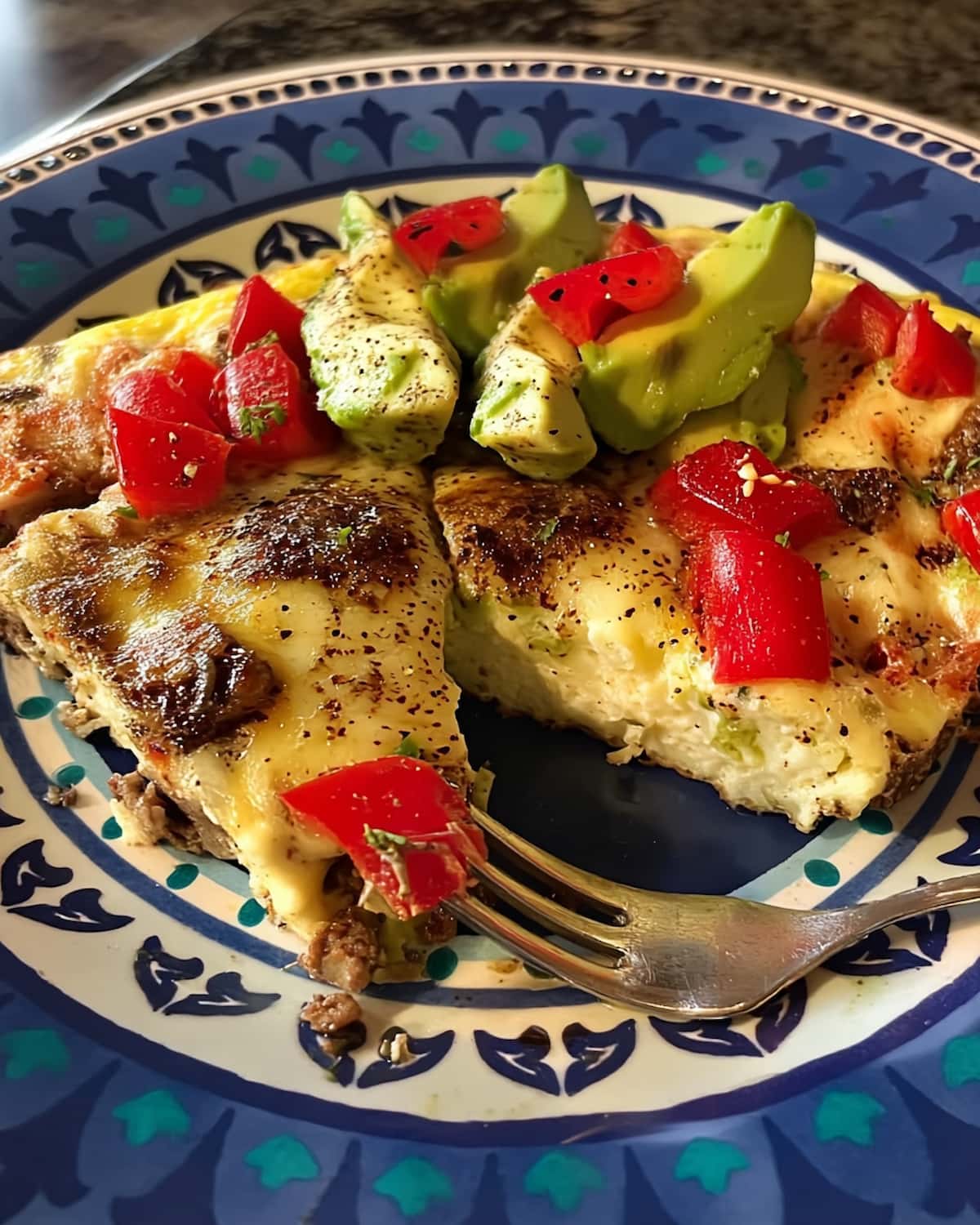 Steak and Eggs Frittata Meal Prep slice topped with melted cheese, diced tomatoes, and avocado.