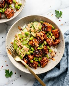 Sriracha Salmon Bowl with sticky honey glaze, rice, cucumber, edamame, and avocado in a meal prep bowl